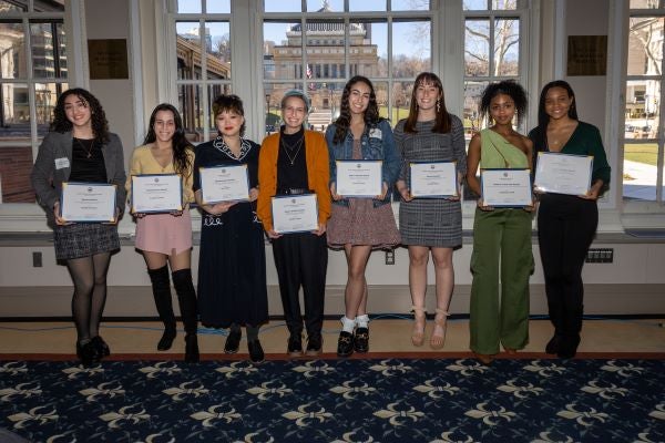 Eight students pose with student awards in front of a window