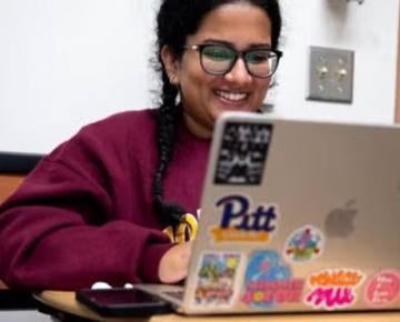 A student smiles while reviewing notes on her laptop