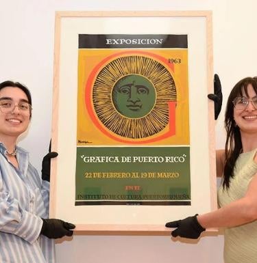 Two students hold a framed graphic design poster with image of a sun