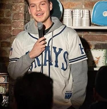 Man stands against a brick wall holding a microphone