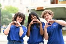 Three students make heart shapes with their hands in front of a fountain