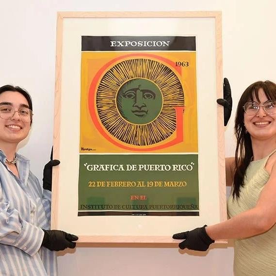 Two students hold a framed graphic design poster with image of a sun