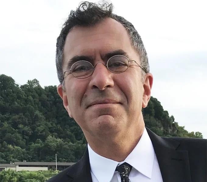 Jeff Aziz, man with oval wire framed glasses stands outside