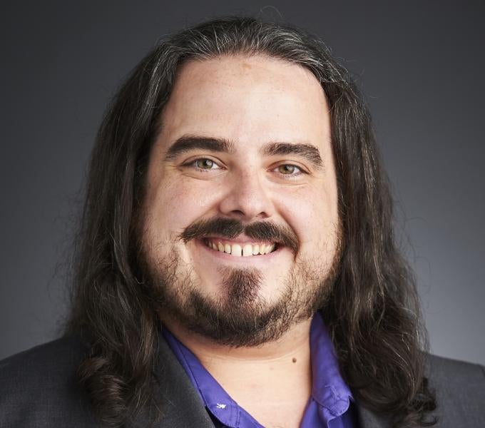 Smiling man with shoulder-length dark hair and beard